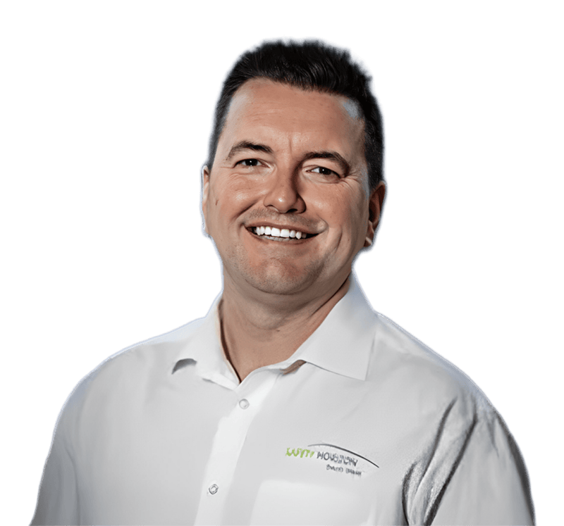 A smiling man with short dark hair wearing a white shirt featuring a green and black "Witty Houston" logo stands against a transparent background, ready to tackle any concrete project in Bristol, from patios to driveway repairs. | Driveways Plus