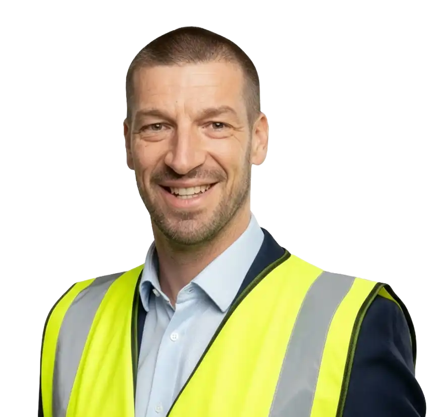 A smiling man wearing a yellow high-visibility safety vest over a light blue collared shirt, representing Driveways Plus as a professional driveway contractor, stands against a white background. | Driveways Plus
