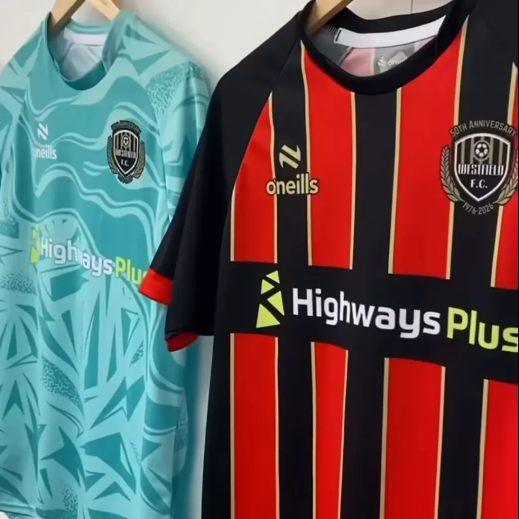 Two football shirts hanging on hangers: one in light blue with abstract patterns and the other in black with red vertical stripes, both displaying the “Highways Plus” sponsor logo and Westfield FC crest for their 50th anniversary. | Driveways Plus