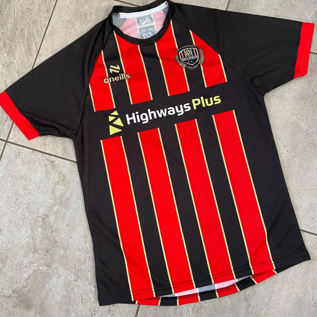 A black and red striped football shirt with yellow accents, featuring the O’Neills logo, Westfield FC club crest, and “Highways Plus” sponsor on the front, celebrating the football club’s 50th anniversary, laid out on a tiled floor. | Driveways Plus