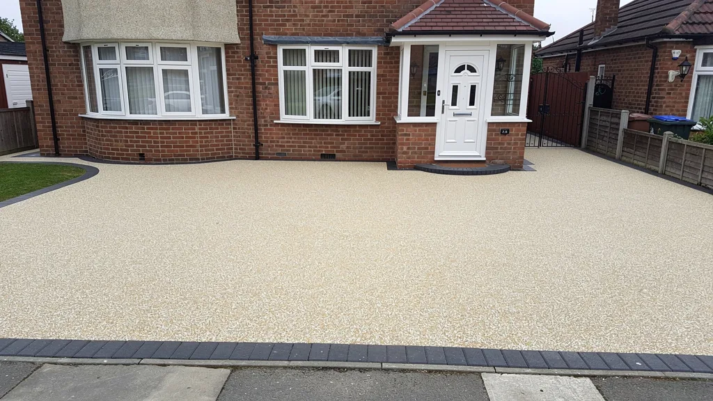 A resin-bound driveway in a warm oyster and cream blend with a charcoal block paving border, in front of a 1930s bay-fronted semi. | Driveways Plus